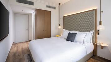 A modern hotel room with a large bed, a wardrobe, a bedside table, and a wall-mounted light fixture.