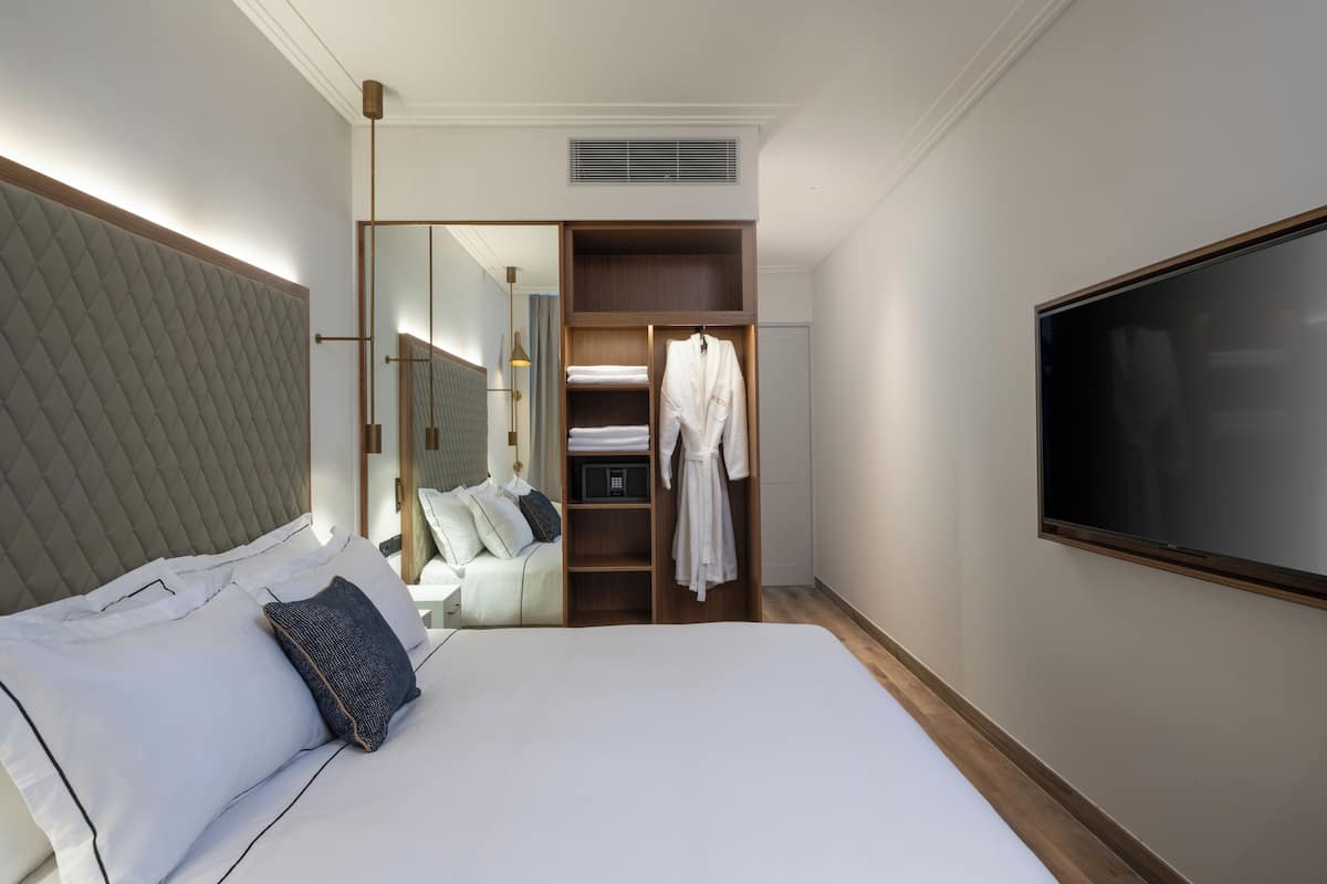 A hotel room with a large bed, a wardrobe, a television, and a mirror.