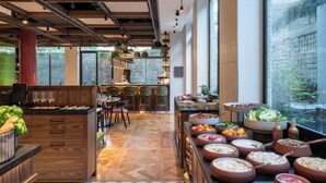 A modern dining area with a long table, multiple seating options, and a variety of food and drink containers. - Hotel Nucha - FATTAL COLORS (Jerusalem)