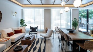 A modern living room with a sofa, chairs, a dining table, and a large window. - Hotel Nucha - FATTAL COLORS (Jerusalem)