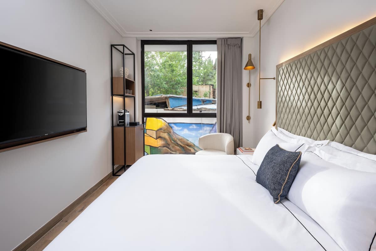 A hotel room with a large bed, a flat-screen TV mounted on the wall, a view of a swimming pool, and a window with curtains.