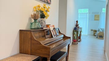 A piano with a decorative vase and books, a wooden bench, and a painting of a sunset on the wall.