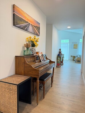 A piano with a decorative vase and books, a wooden bench, and a painting of a sunset on the wall. -  BRANCH HOUSE WALK TO MARKET, LAKE. (Anchorage)