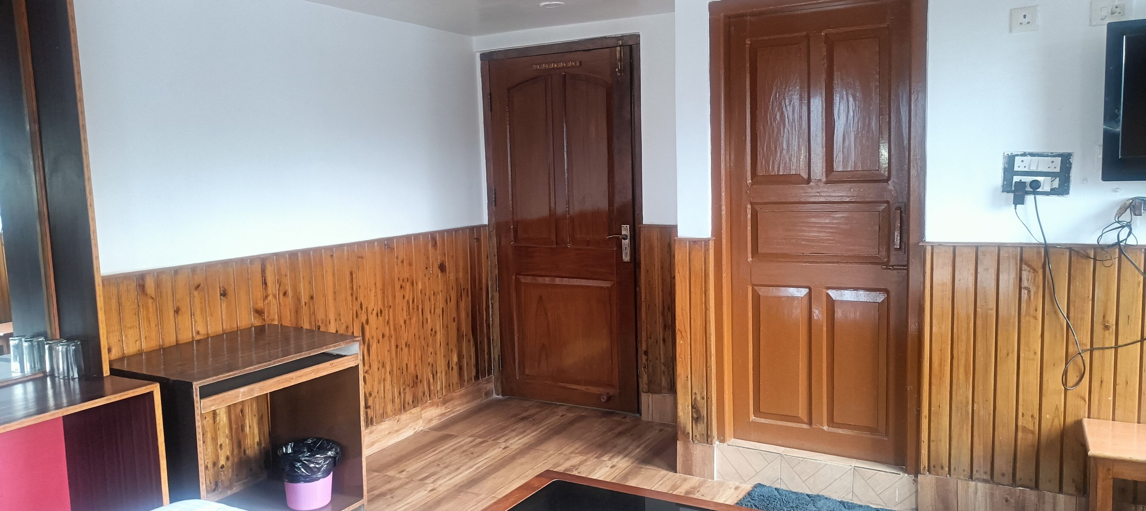 Un pasillo con revestimiento de madera, una puerta cerrada, una mesita con vasos y un cesto de basura.