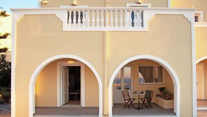 A building with a beige facade, white arches, and a balcony with seating. - Ostria, Pithos Apartments (Thira - Santorini)