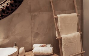 Ein Badezimmer mit einem hölzernen Handtuchhalter, der zwei Handtücher trägt, einem weißen Waschbecken und einer dekorativen Vase.