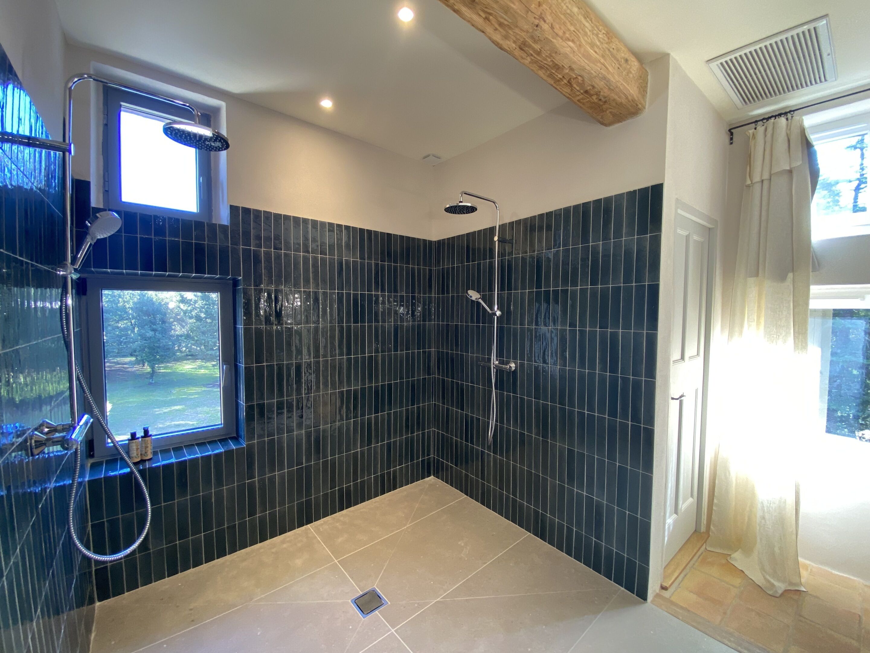 Un baño moderno con paredes de azulejos oscuros, una ducha con cabezal de ducha manual y una ventana que ofrece vistas al exterior.