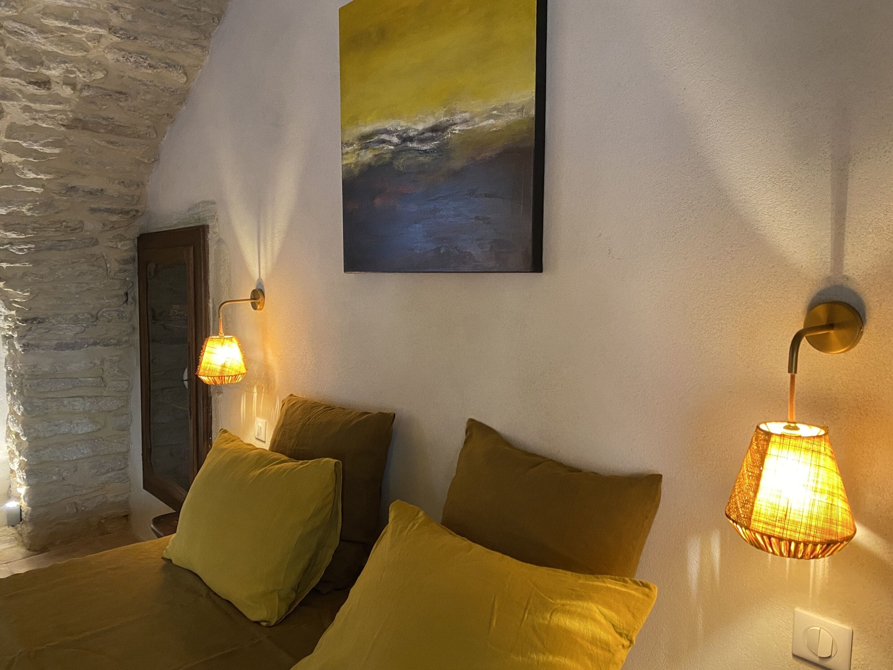 Una habitación acogedora con pared de piedra, cama con almohadas amarillas y dos lámparas de pared.
