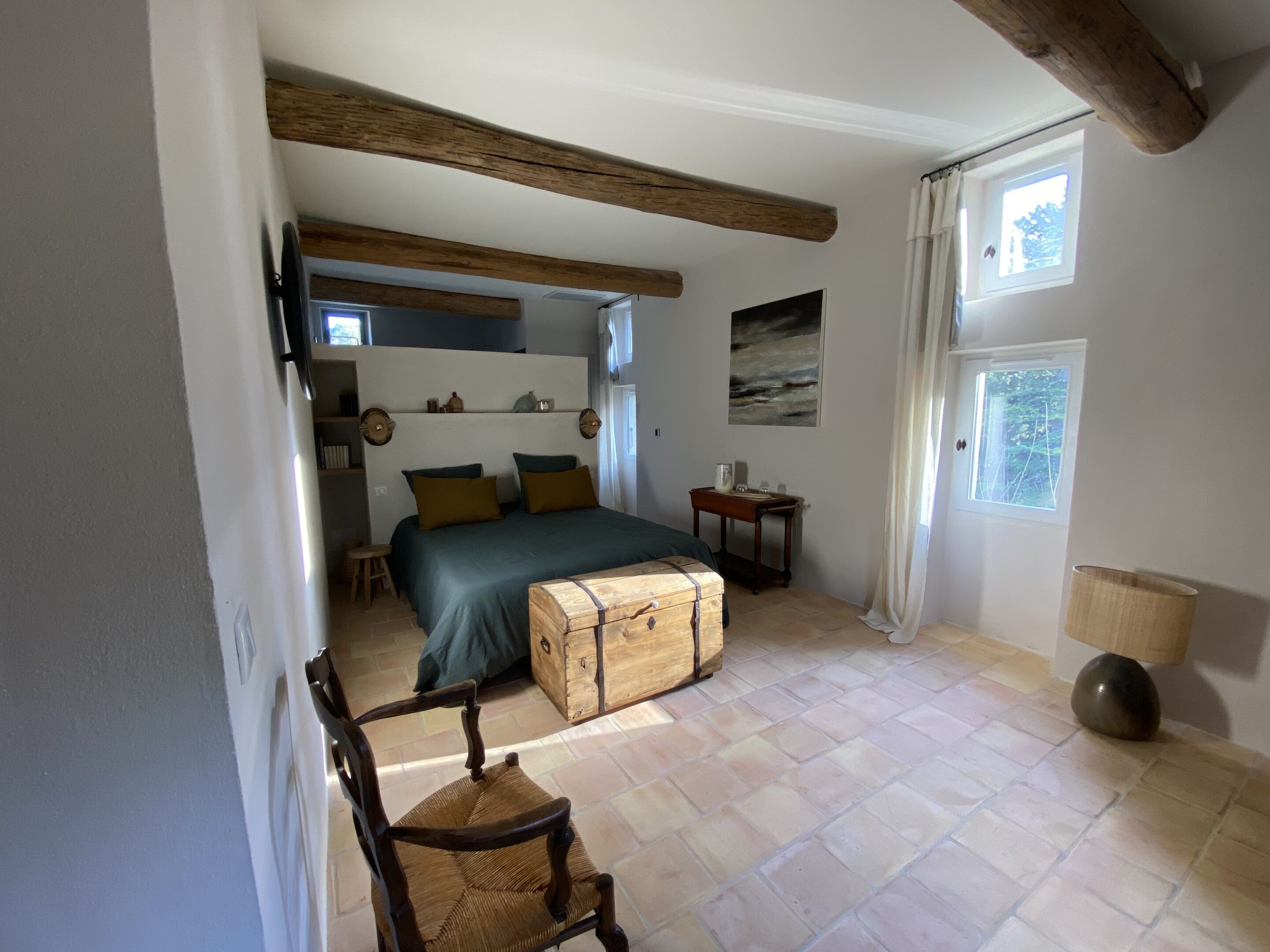 A bedroom with a bed, a wooden chest, a chair, a small table, and a window.