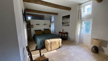 A bedroom with a bed, a wooden chest, a chair, a small table, and a window.