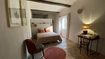 A bedroom with a bed, a desk, a chair, a red rug, and a window with curtains.