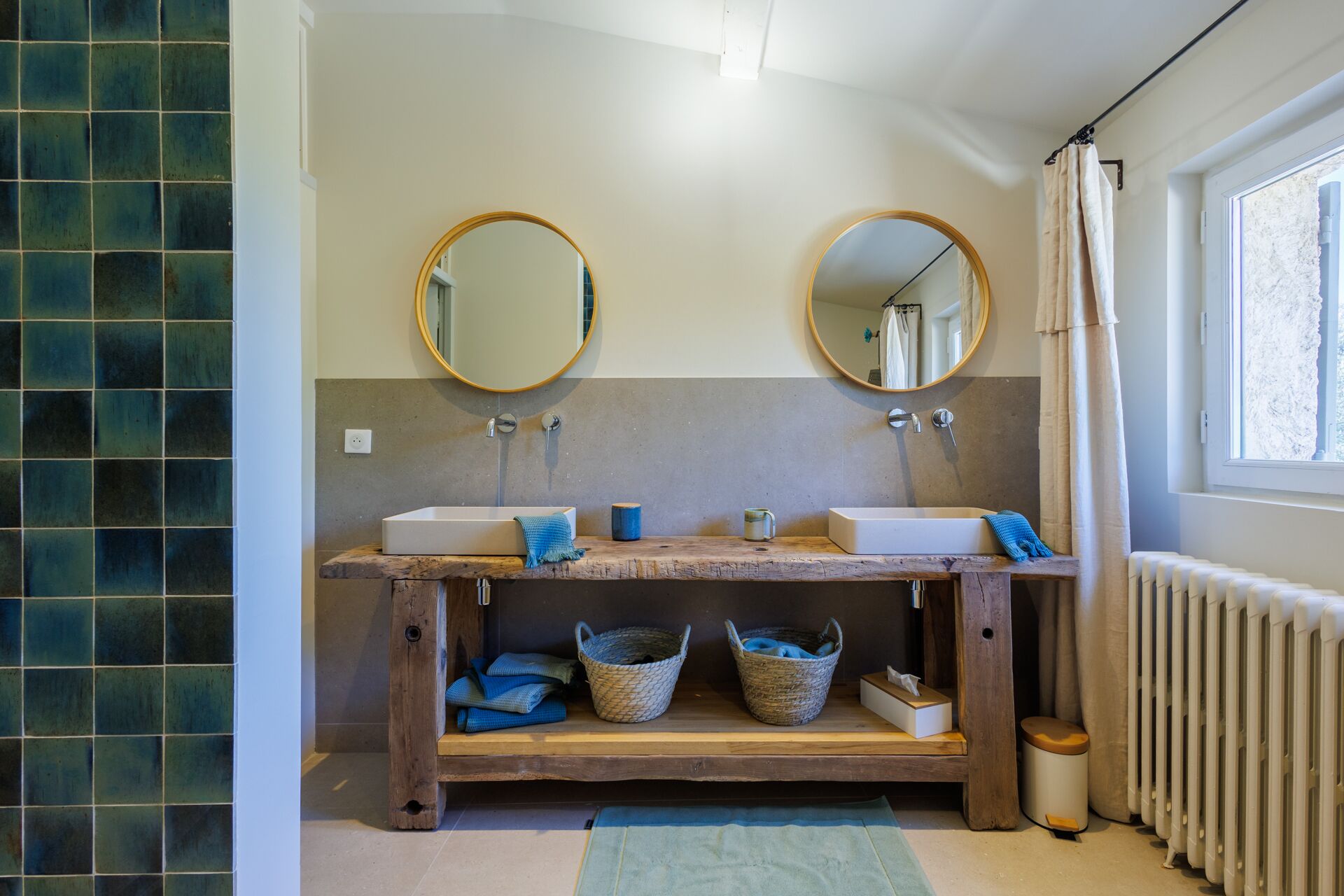 Un baño con dos lavamanos, dos espejos redondos, un tocador de madera y una ventana con cortina.