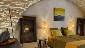 Un dormitorio acogedor con pared de piedra, cama con ropa de cama verde, dos lámparas de noche y una mesita con un objeto decorativo.