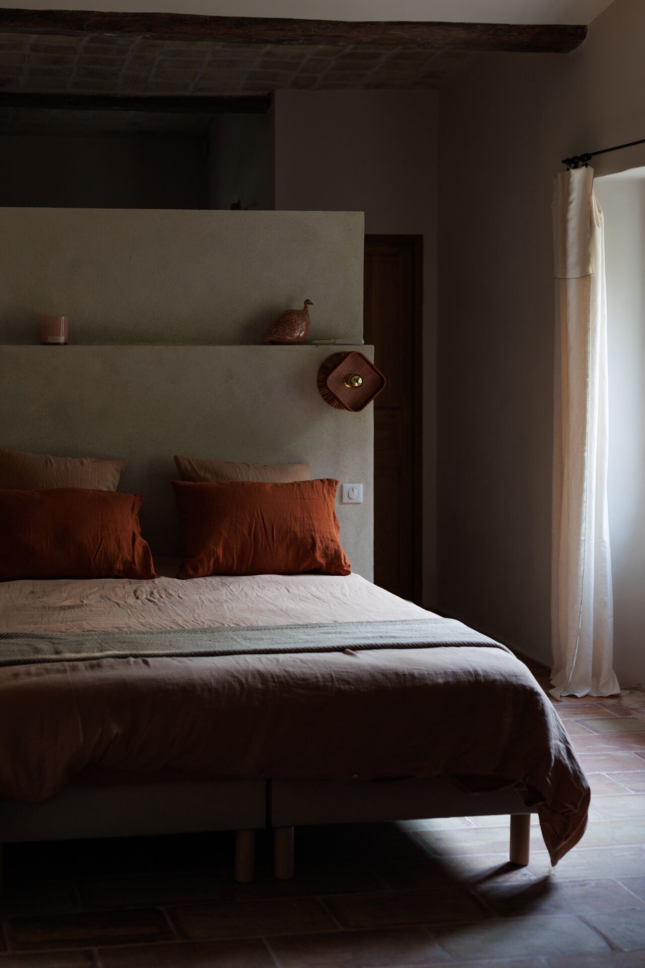 A bedroom with a large bed, two pillows, a nightstand, and a wall-mounted shelf with a decorative item.