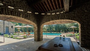 Un espacio al aire libre cubierto con piscina, paredes de piedra y mobiliario de madera.