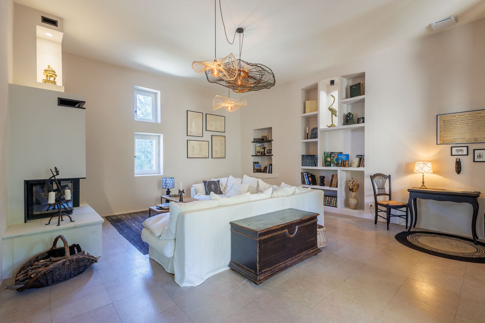 Uma sala de estar ampla com um sofá branco, um baú de madeira e uma estante cheia de livros e objetos decorativos.