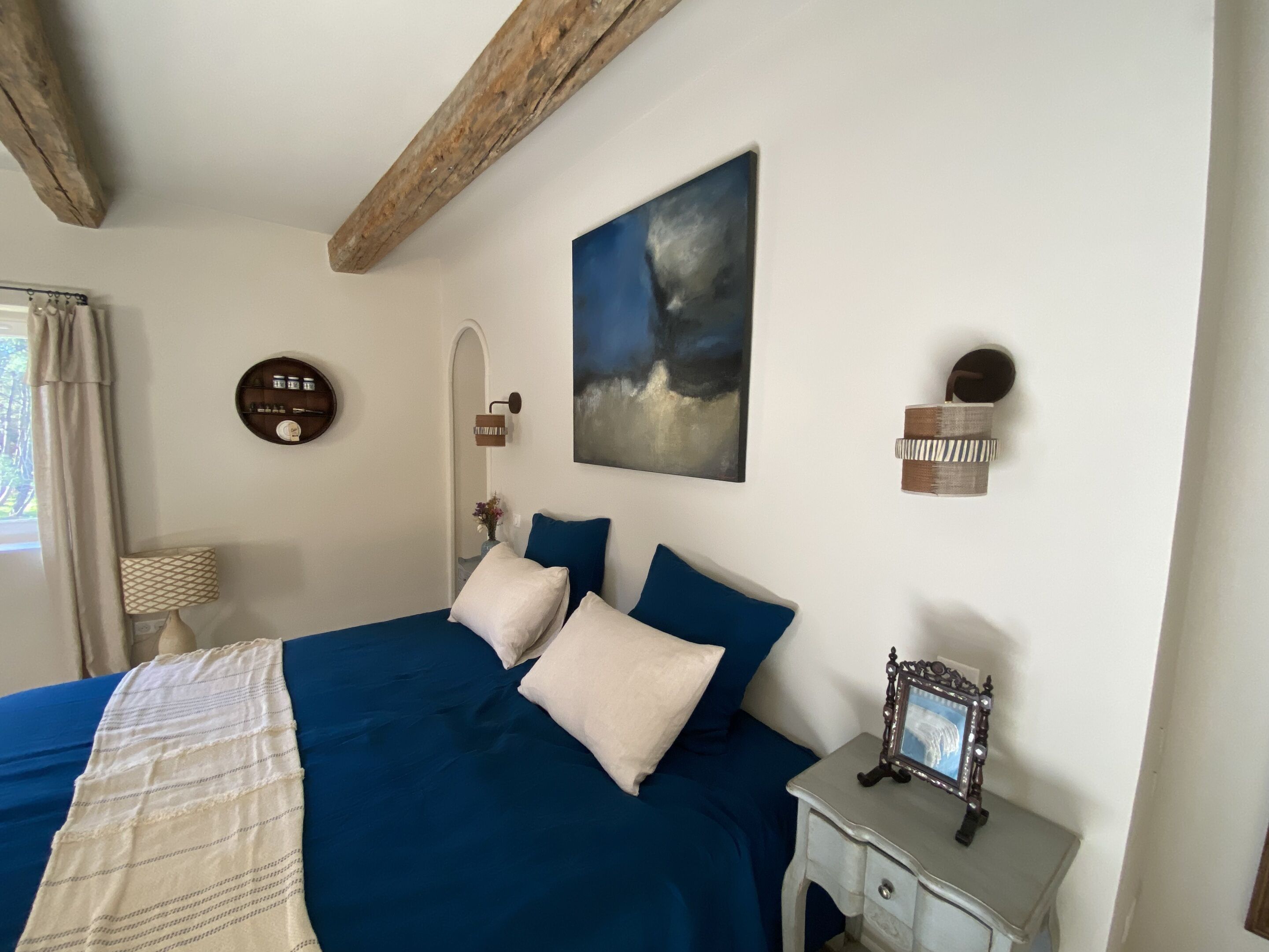 Un dormitorio con una cama, una mesita de noche, un estante en la pared y un cuadro.