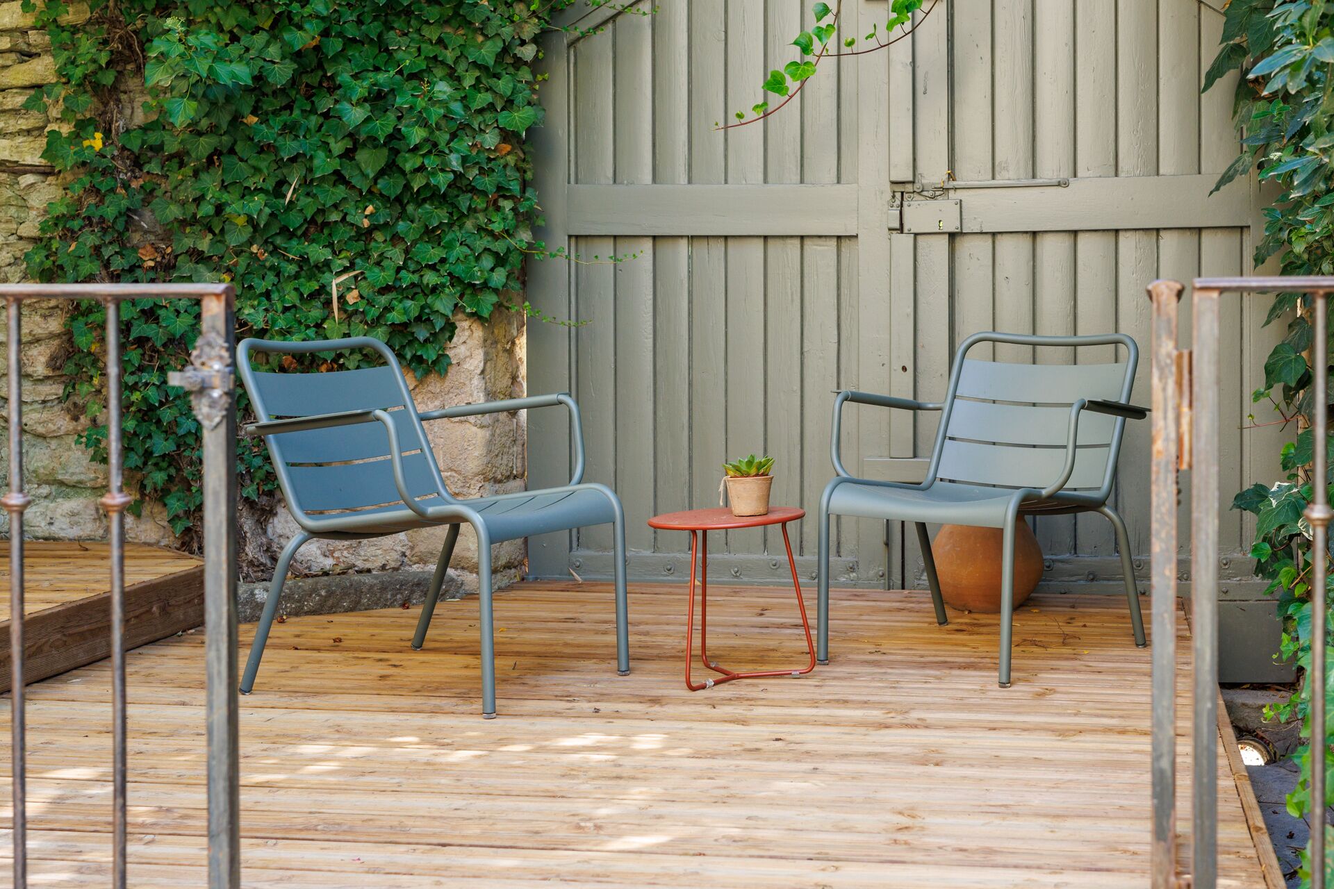 A wooden deck with two metal chairs and a small round table, surrounded by a stone wall and a wooden fence.