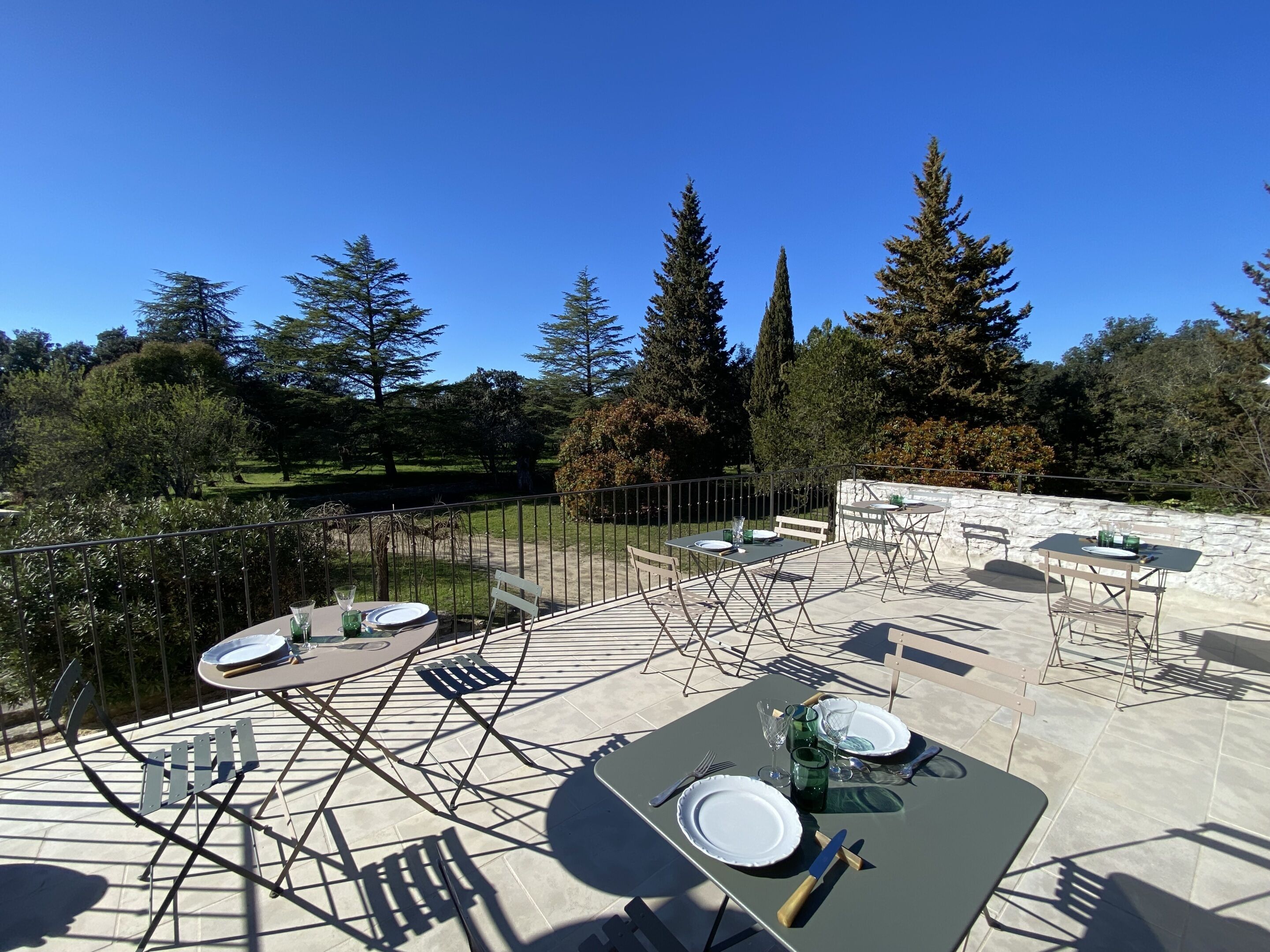 Zona pranzo all'aperto con tavoli e sedie, circondata da un muro in pietra e alberi.