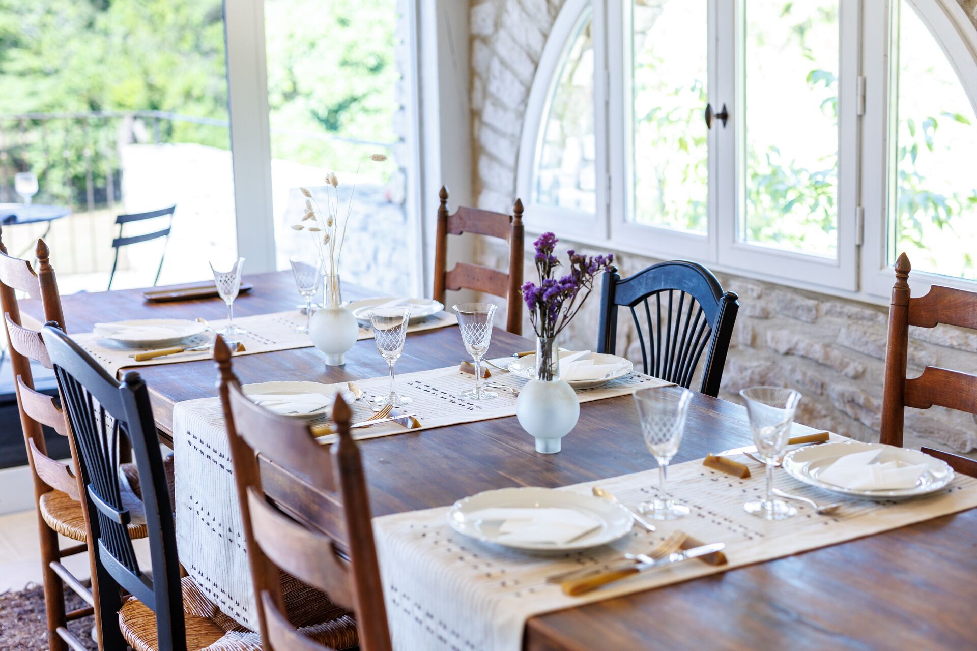 Une table à manger dressée avec de l’argenterie blanche, des couverts et de la verrerie, entourée de chaises en bois dont les assises sont en osier tressé.