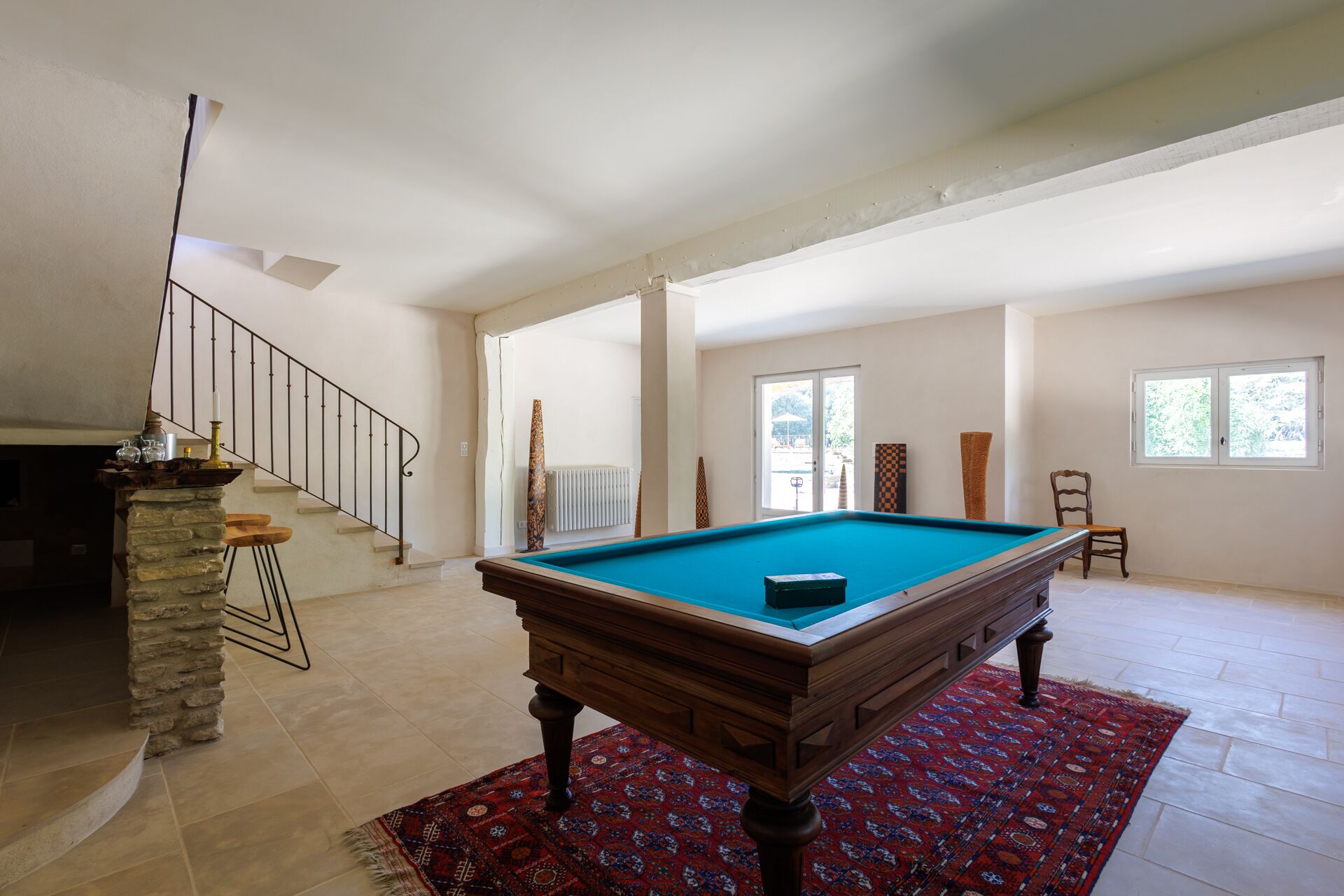A spacious room with a pool table, a staircase, and a view of the outdoors.
