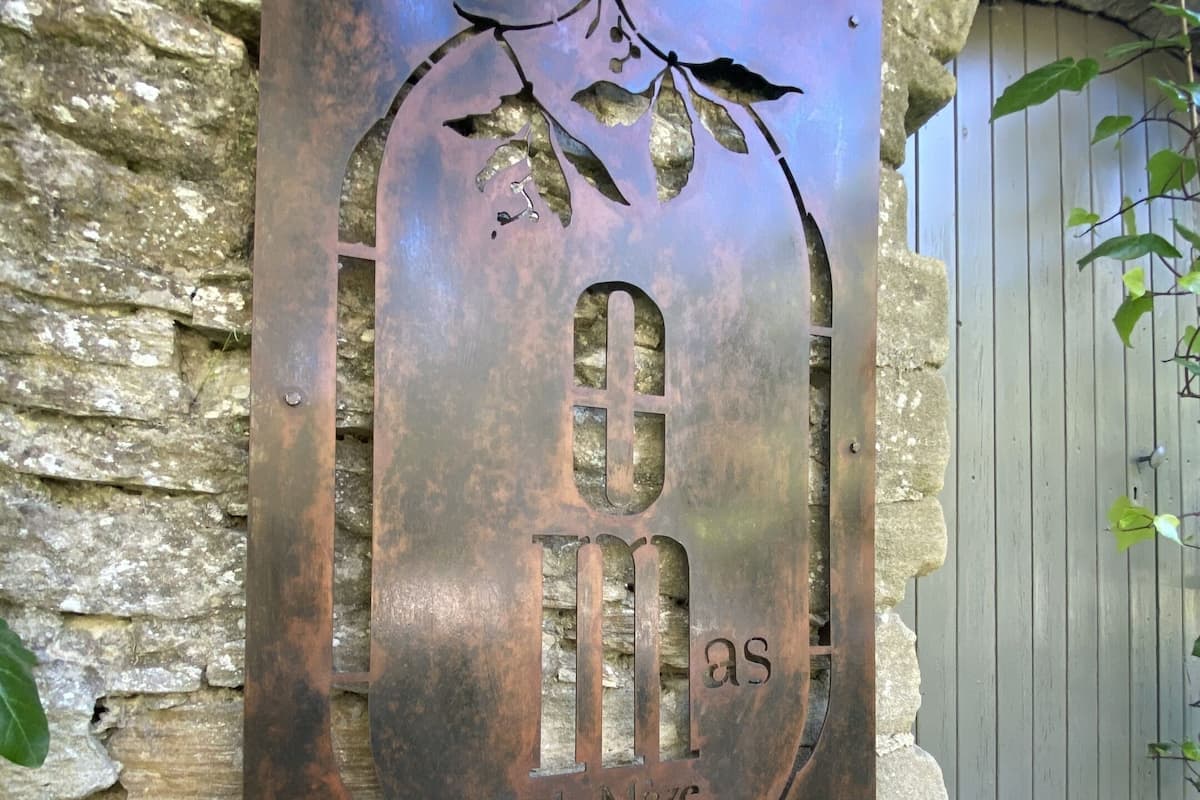 A metal plaque with a grapevine design and the inscription "de Maza".