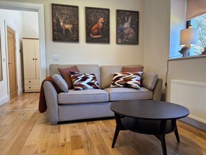 Un salon avec un canapé gris, deux coussins décoratifs à motifs, une table ronde noire et trois tableaux représentant des animaux, accrochés au mur.