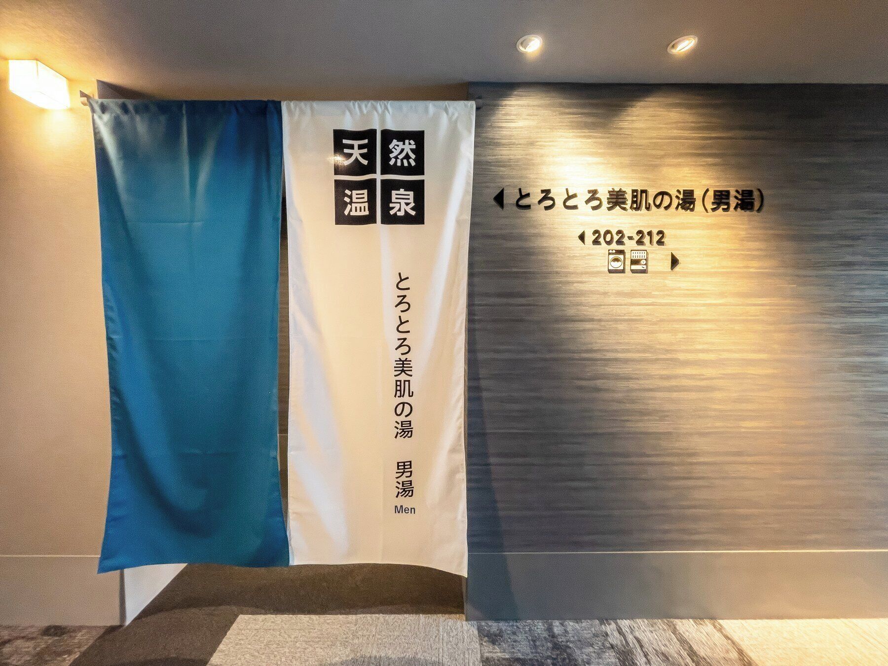 A hotel reception area with a blue curtain, a white sign with Japanese text, and a wall with a metallic finish and directional arrows.