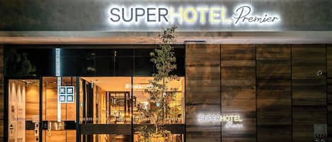 The exterior of the SuperHotel Premier with a modern design, featuring a prominent entrance and a small garden area in front.