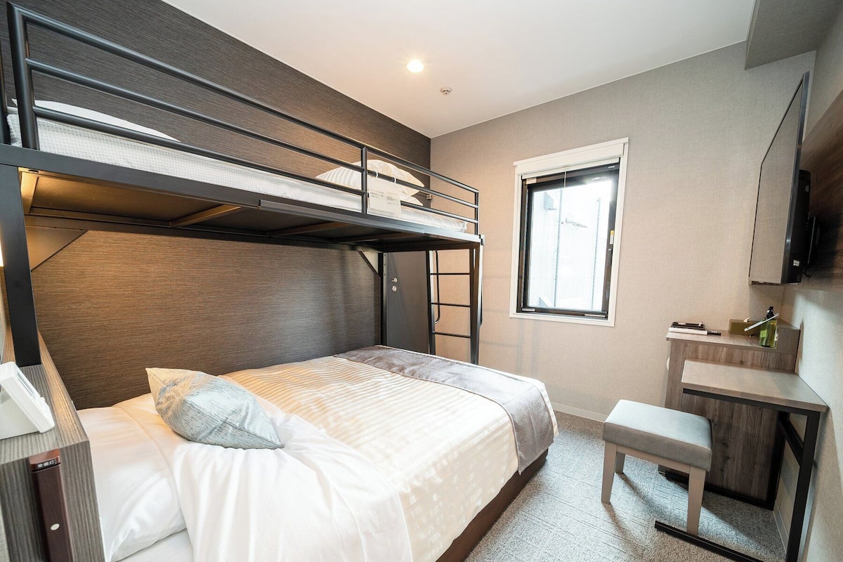Une chambre d’hôtel compacte comprenant un lit superposé, un petit bureau, une fenêtre et un téléviseur à écran plat.
