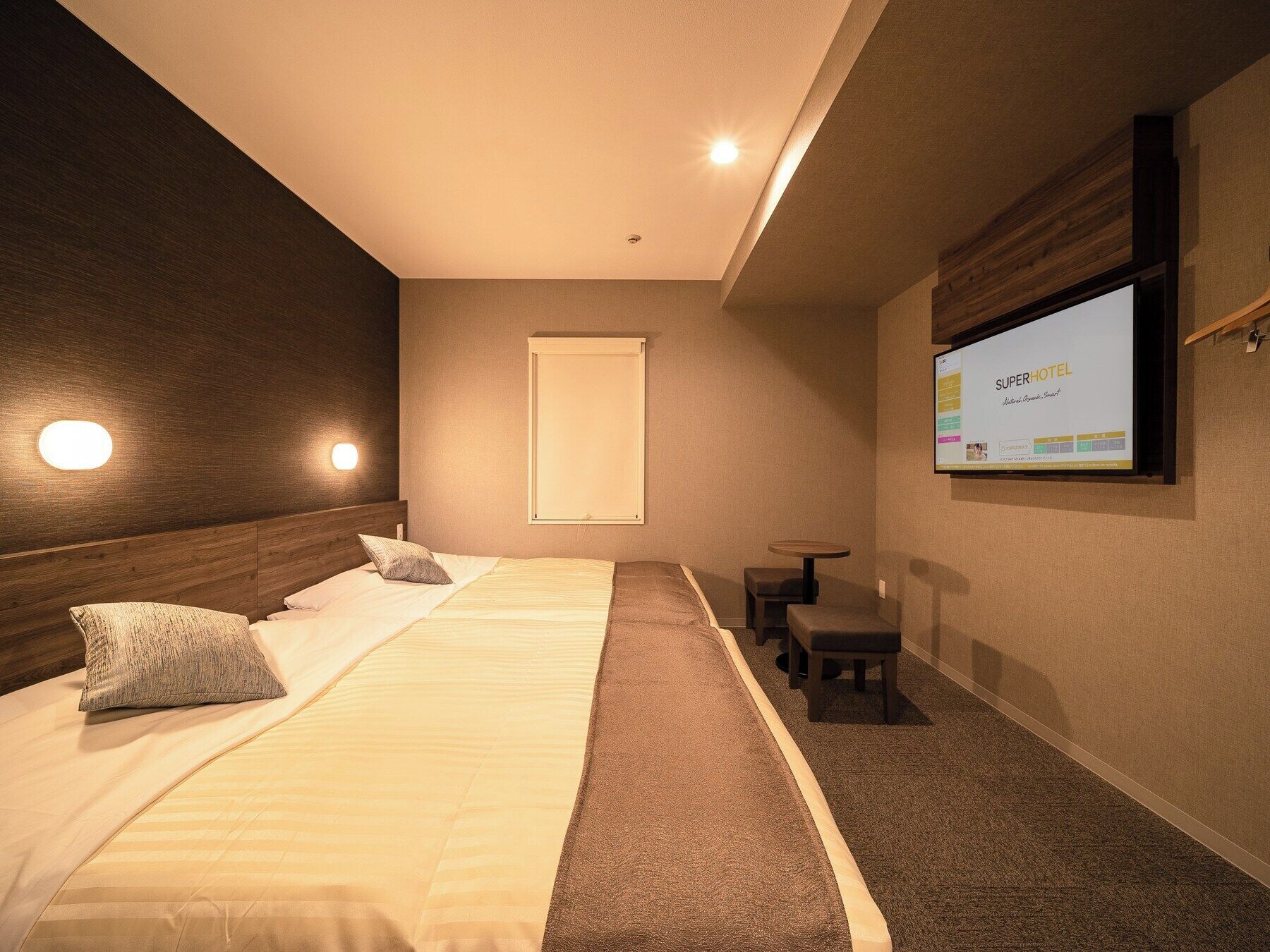 A hotel room with a large bed, a small table, and a TV screen displaying the hotel's name.