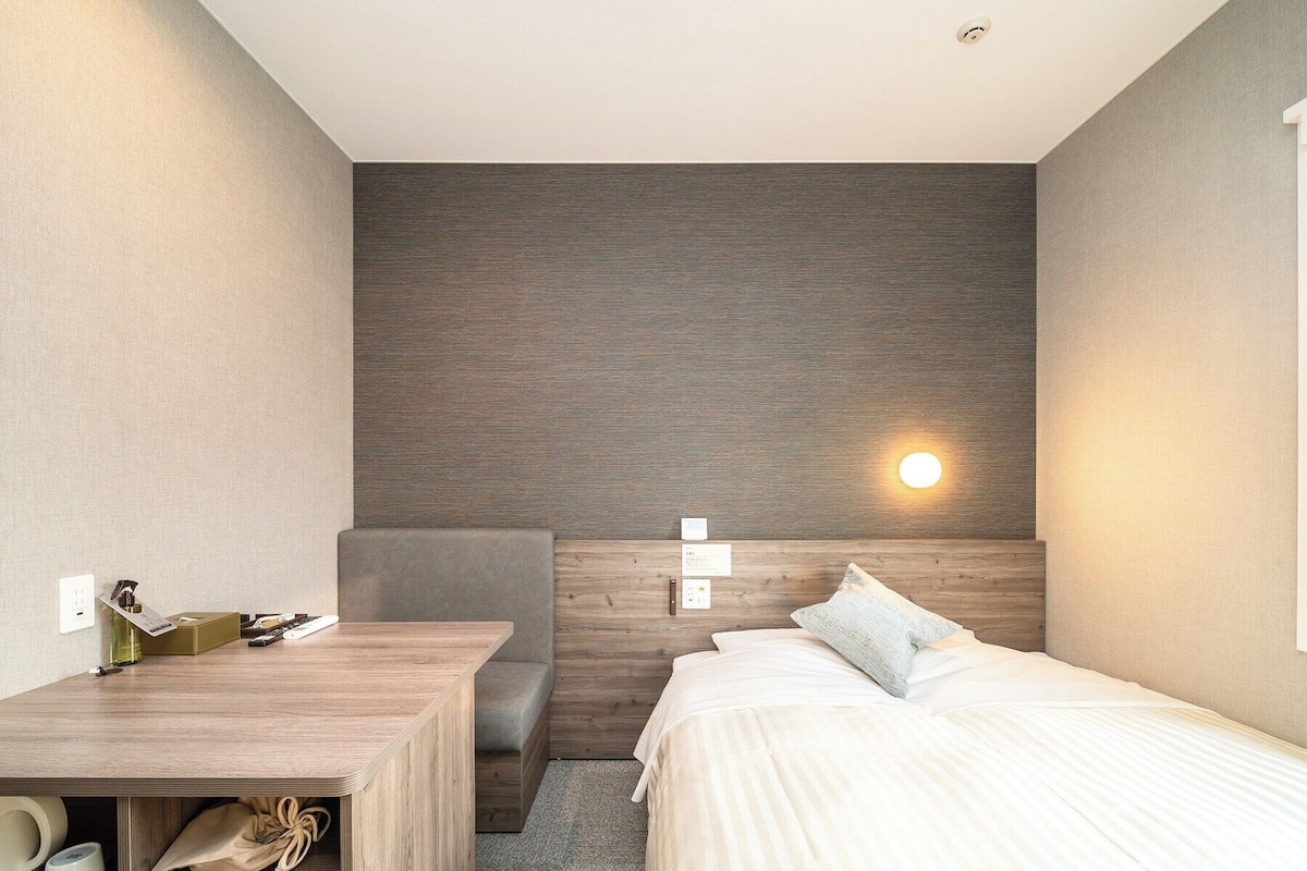 Une chambre d’hôtel moderne avec une tête de lit en bois, une table de chevet, une chaise et un lit avec une literie blanche.