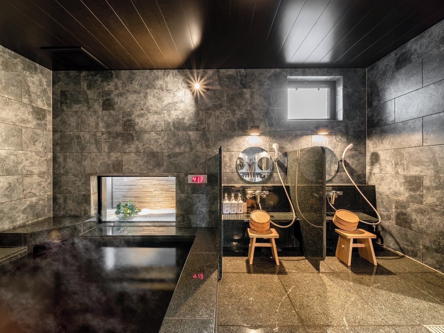 A modern sauna room with stone walls, a wooden bench, and a small window.