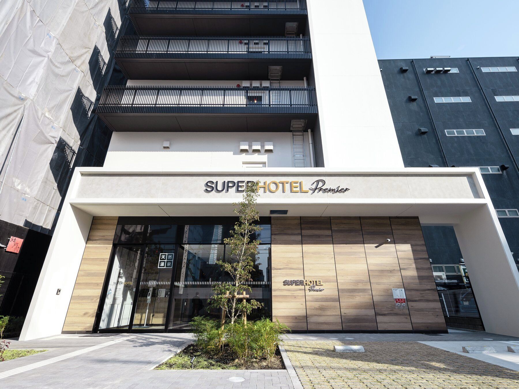 A hotel entrance with a modern facade, a sign reading "SuperHotel Premier," and a small tree in the foreground.