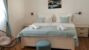 A bedroom with a bed, bedside tables, a hanging light fixture, a chair, and a round ottoman.
