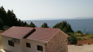 A single-story building with a red-tiled roof, situated on a hillside with a view of the sea.