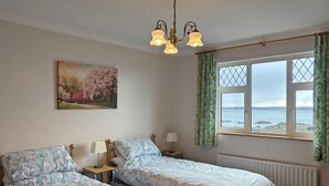 A bedroom with two beds, a chandelier, a window with curtains, a radiator, and a painting on the wall. - Cottage 467 - Kilkerrin - sleeps 8 guests  in 4 bedrooms (Kilkerrin)