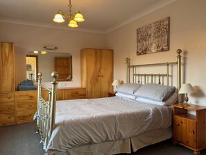 A bedroom with a bed, wooden wardrobe, a mirror, and a painting on the wall.