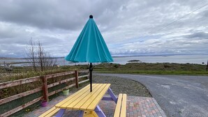 A picnic table with a blue umbrella, a wooden fence, and a view of the sea. - Cottage 467 - Kilkerrin - sleeps 8 guests  in 4 bedrooms (Kilkerrin)
