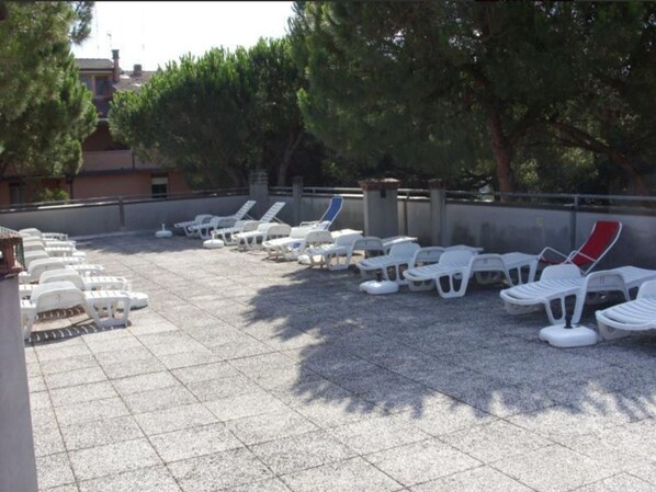Une terrasse sur le toit, avec des rangées de chaises longues blanches et quelques-unes rouges, entourée d’arbres et d’immeubles.