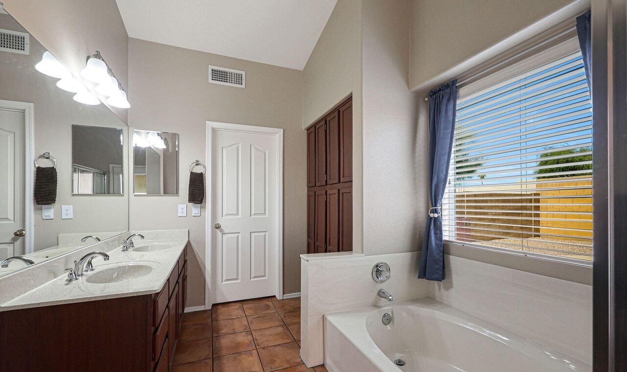 A bathroom with a double sink vanity, a bathtub, and a large mirror.