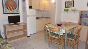A compact kitchen with a dining table, chairs, a refrigerator, and a television. - Welcoming apartment in Rosolina (Rosolina Mare)