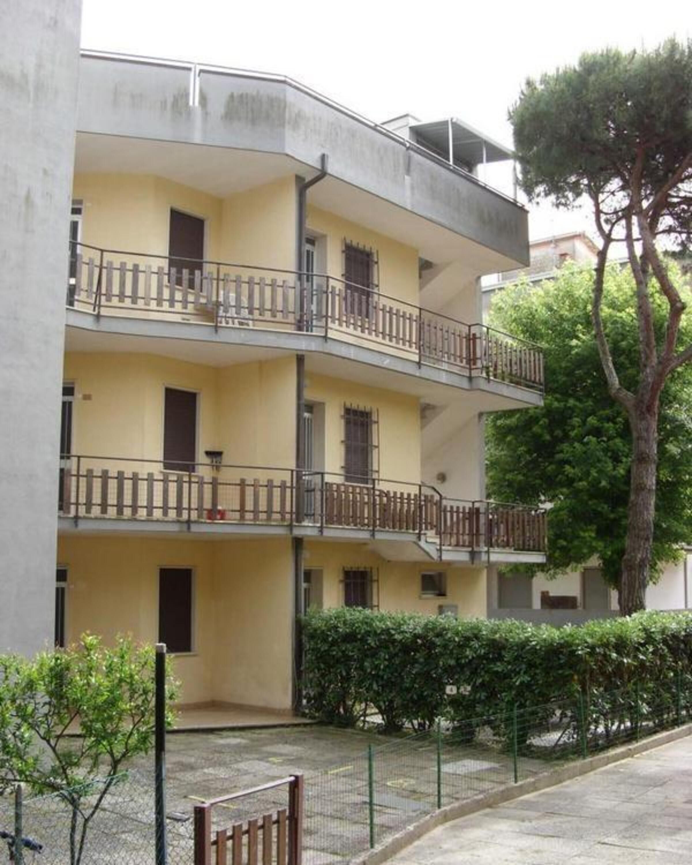 A multi-story residential building with balconies, a paved courtyard, and a tree.