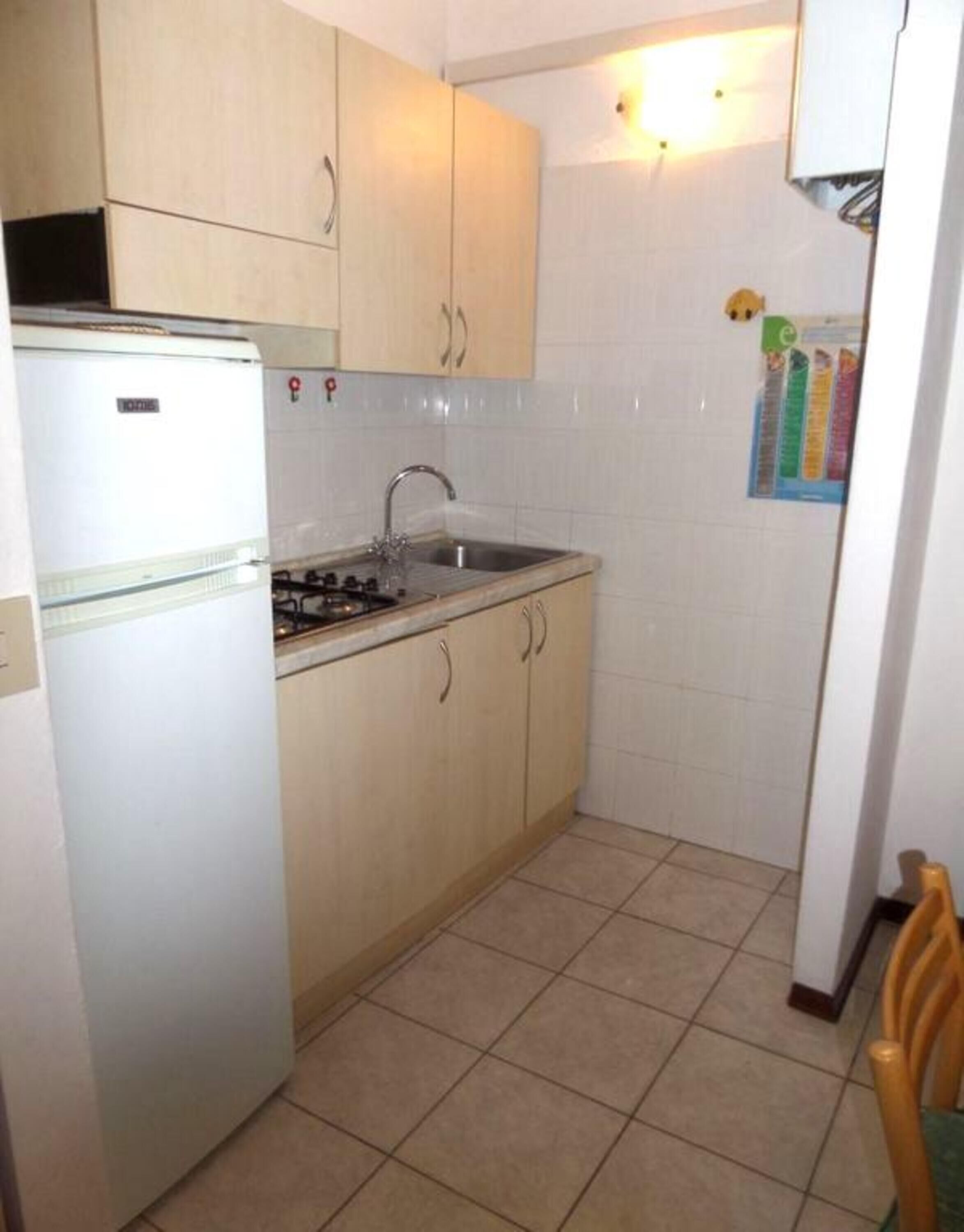 A compact kitchen with a white refrigerator, a gas stove, a sink, and light-colored cabinets.