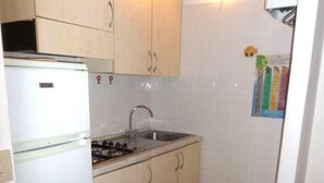 A compact kitchen with a white refrigerator, a gas stove, a sink, and light-colored cabinets. - Welcoming apartment in Rosolina (Rosolina Mare)