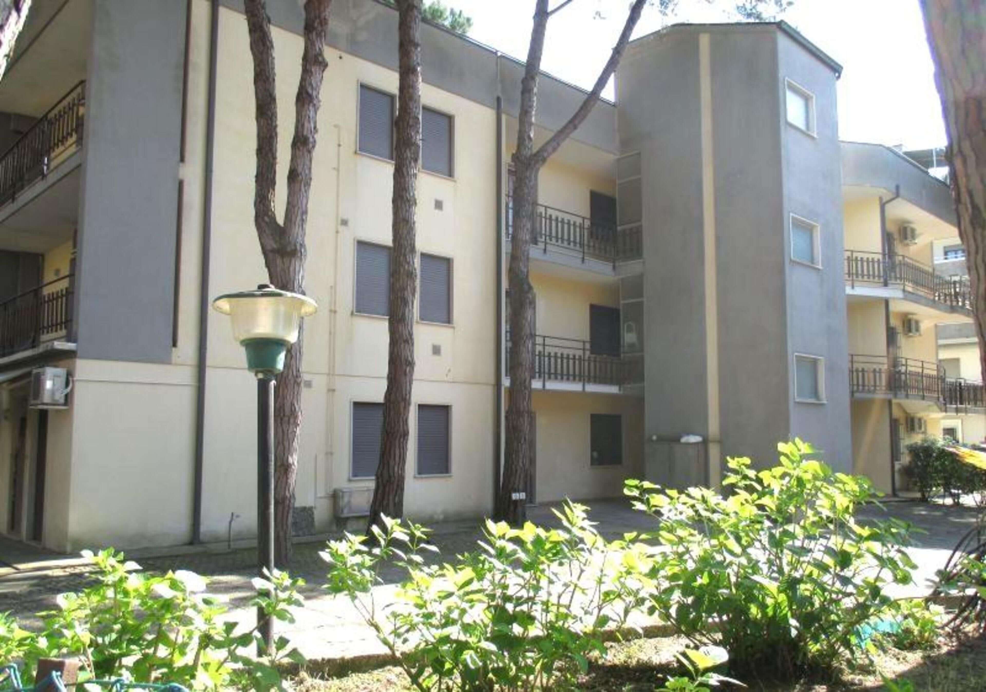 A multi-story residential building with balconies, a street lamp, and trees in the foreground.
