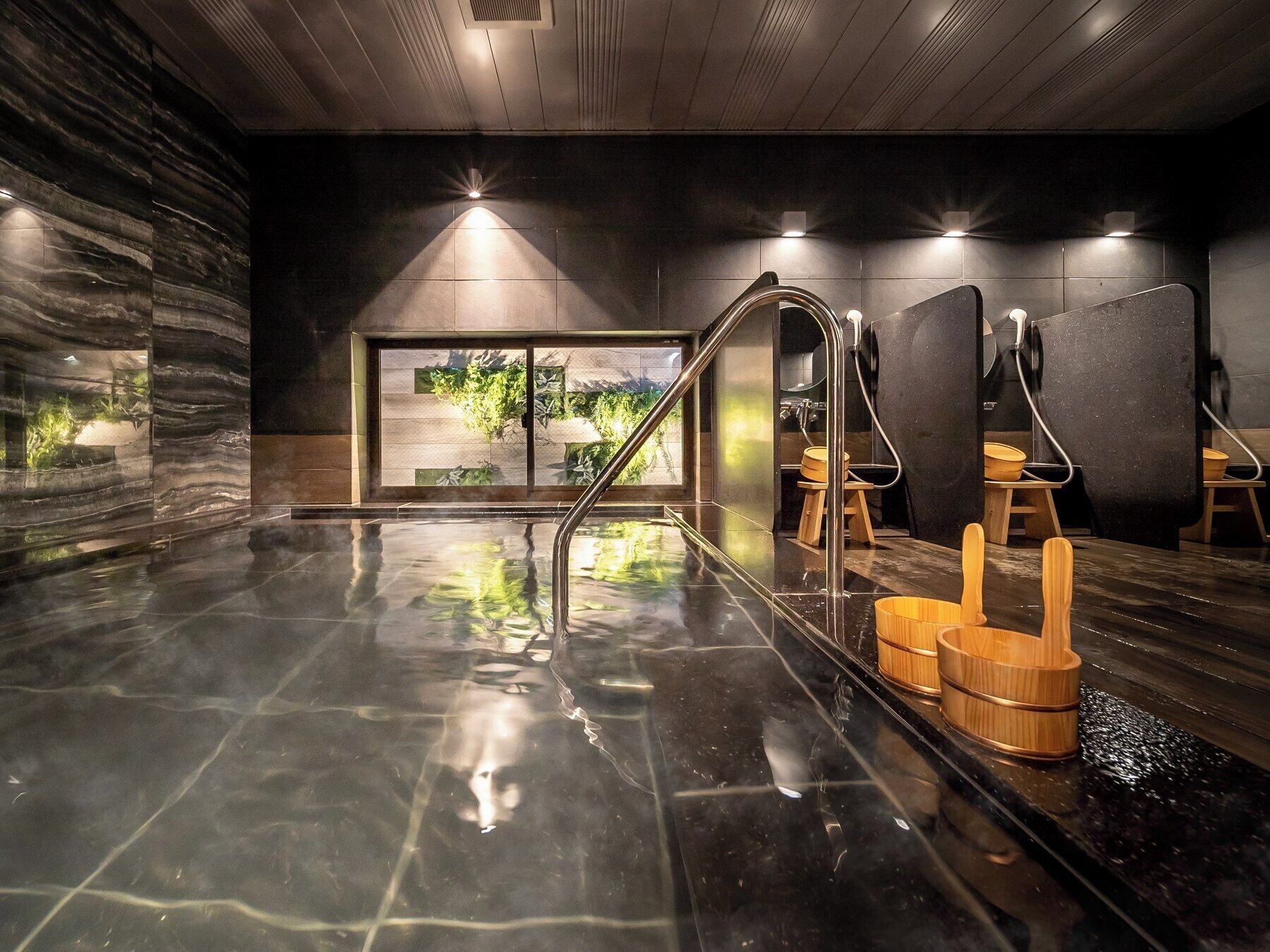 Een moderne spa met vloerverwarming, houten krukken en uitzicht op groen.