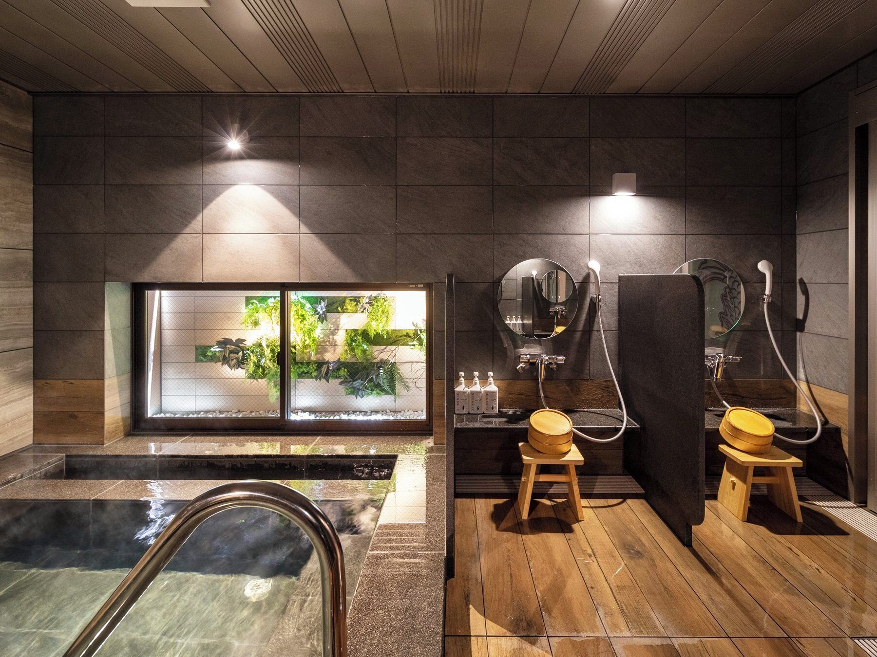 A modern spa with a hot tub, wooden stools, and a large window with plants.