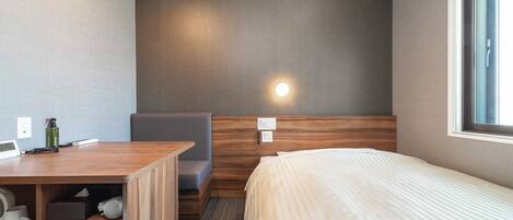 A hotel room with a bed, a desk, a chair, and a small table.
