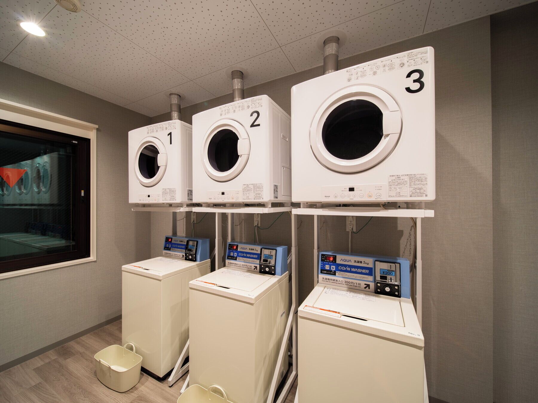A laundry facility with three stacked washing machines and two coin-operated dryers.